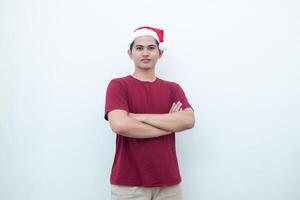 Young Asian man wearing a Santa Claus hat crossing his arms while smiling, shock and laughing with a white background for visual communication photo