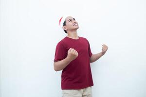 joven asiático hombre vistiendo un Papa Noel claus sombrero agarre ambos manos con entusiasmo y ira aislado por un blanco antecedentes para visual comunicación foto