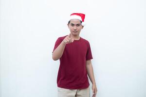 Young Asian man wearing a Santa Claus hat smiling, shock and pointing to her side isolated by white background for visual communication photo