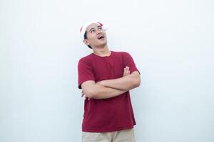 Young Asian man wearing a Santa Claus hat crossing his arms while smiling, shock and laughing with a white background for visual communication photo