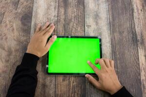 Mock up of a hand holding an iPad tablet with a greenscreen against a wooden texture background photo