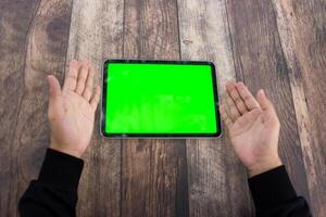 Mock up of a hand holding an iPad tablet with a greenscreen against a wooden texture background photo