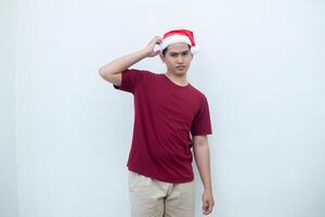 Young Asian man wearing a Santa Claus hat expressing confusion, thinking, and then having an idea, isolated by a white background for visual communication photo