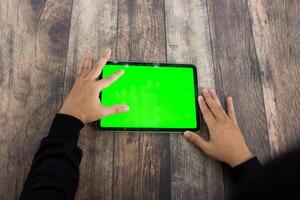 Mock up of a hand holding an iPad tablet with a greenscreen against a wooden texture background photo