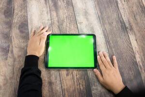 Mock up of a hand holding an iPad tablet with a greenscreen against a wooden texture background photo