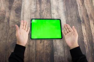 Mock up of a hand holding an iPad tablet with a greenscreen against a wooden texture background photo