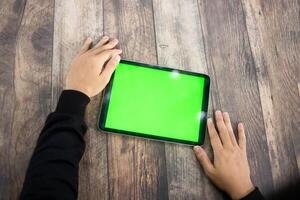 Mock up of a hand holding an iPad tablet with a greenscreen against a wooden texture background photo