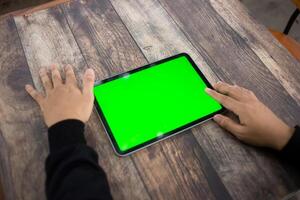 Mock up of a hand holding an iPad tablet with a greenscreen against a wooden texture background photo