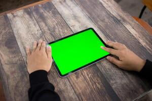 Mock up of a hand holding an iPad tablet with a greenscreen against a wooden texture background photo