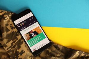 KYIV, UKRAINE - 4 MAY, 2023 ukrainian news portal on smartphone screen with ukrainian flag and camouflage fabric photo