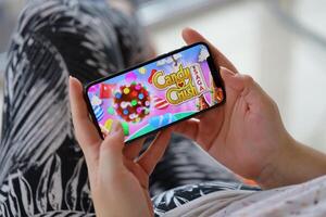 Candy Crush Saga mobile iOS game on iPhone 15 smartphone screen in female hands during mobile gameplay photo