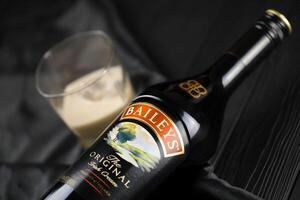 KYIV, UKRAINE - MAY 4, 2022 Baileys original alcohol bottle on wooden table with black fabric photo