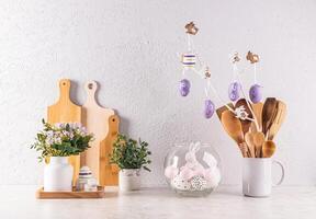 Decorating the kitchen countertop for the Easter holiday. Kitchen wooden utensils, potted plants, a branch with lilac eggs. Front view. Eco style photo