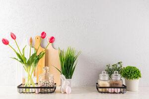 Stylish kitchen background decorated for Easter holiday. vase with tulips, potted plants, eggs on stands, ceramic rabbits. Front view. photo