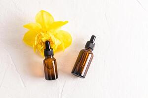 Natural cosmetic product in two amber glass bottles with dropper on white embossed background with yellow bright narcissus flower. Care, beauty photo