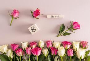 Beautiful festive background for International Women's Day on the eighth of March with delicate white and pink roses and a wooden calendar. border. photo