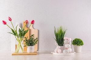 Beautiful festive decoration of the kitchen countertop for Easter Day. vase with tulip, green plants, eggs with pattern in high glass, easter bunnies. photo