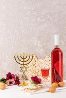 festivo composición para el judío Pascua. un botella de comestible según la ley judía vino, matzot, un cristal vaso de vino, un tradicional oro candelero Menorah foto