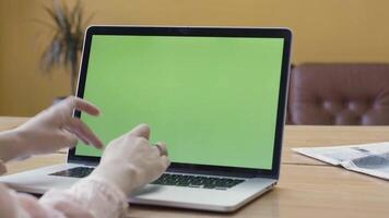 Over the shoulder view of a woman hands using laptop with green screen. Stock footage. Female hands typing on a laptop keyboard, chromakey business, communication, freelance and internet concept video