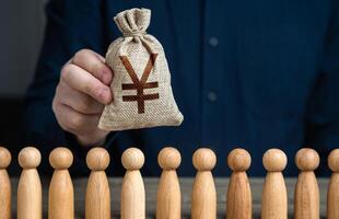 A man holds a chinese yuan or japanese yen money bag above the crowd. Deposits and loans. Budgetary funds for social policy. Social politics. Salaries. Crowdfunding and fundraising. photo