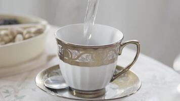 Close up of porcelain mug of white and golden colors standing on the table with hot tea. Stock footage. Hot water is poured into a ceramic cup on the table. video