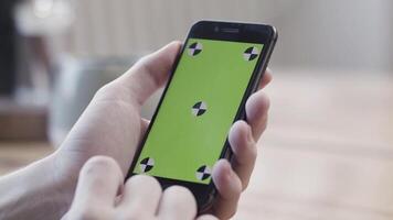 Close up of hands using smartphone with green screen, sliding and tapping on blurred kitchen table background. Stock footage. Man hands holding mobile phone with chroma key. video