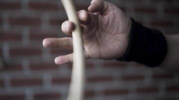 proche en haut de homme main avec noir en tissu bracelet sur le sien poignet en portant pilon et tournant il avec le Aidez-moi de le sien les doigts sur une rouge brique mur Contexte. action. musical instruments concept. video