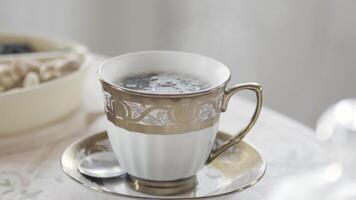 Close up of elegant porcelain cup of hot tea with steam standing on the table in light room. Stock footage. Aristocratic morning breakfast. video