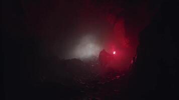 silhouette di un' geologo l'esame buio grotta, Tenere rosso segnale bagliore. azione filmato. scienziato uomo esplorando pietroso vecchio tunnel , natura e paleontologia concetto. video