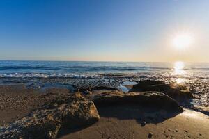 Scenic rock formation on a beach with sunset and sea waves photo