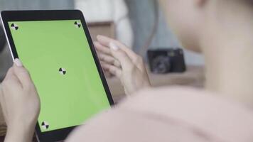 kant visie van een vrouw Holding tablet pc met groen scherm Aan houten tafel achtergrond. voorraad filmmateriaal. dichtbij omhoog van een meisje gebruik makend van ipad met chroma sleutel. video