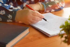 hand holding red pen over blurred paperwork for proofreading photo