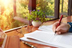 hand holding red pen over blurred paperwork for proofreading photo