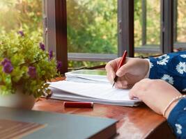 hand holding red pen over blurred paperwork for proofreading photo