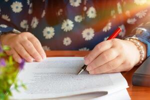 hand holding red pen over blurred paperwork for proofreading photo