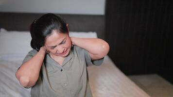 cansado mujer sufrimiento desde cuello dolor en el Mañana después dormido en un incómodo almohada a hogar o hotel habitación. video
