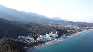 Video. Antenne Aussicht von Hotel auf Meer Ufer und Berge bedeckt mit Grün Wald, Bäume mit Blau Himmel beim Sonnenaufgang. Video. Antenne Aussicht auf Strand mit Luxus Hotel mit Wald und Berge Hintergrund video