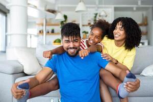 Happy African American dad and mom with excited proud daughter kid, playing flying superhero, reaching arm forward. Cheerful girl playing active game with family at home photo