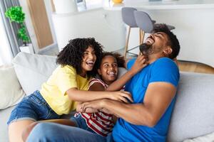 Cheerful people sitting on couch in living room have fun little daughter tickling mother laughing together with parents enjoy free time playing at home. Weekend activity happy family lifestyle concept photo