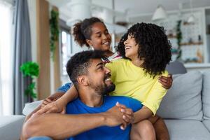 Love And Care. Portrait of cheerful family of three people hugging sitting on the sofa at home. Smiling young girl embracing her parents. photo