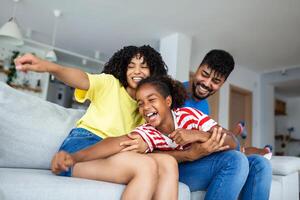 Happy African American dad and mom piggybacking excited proud daughter kid, playing flying superhero, reaching arm forward. Cheerful girl riding fathers back playing active game with family at home photo