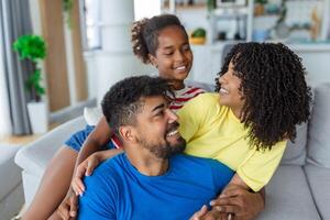 Positive cheerful multi-ethnic family wife husband child sitting together on couch at home. Close up focus on little daughter and beautiful mother. Happy multiracial family concep photo