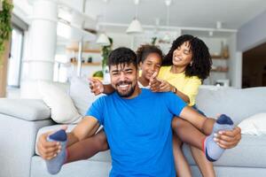 Happy African American dad and mom with excited proud daughter kid, playing flying superhero, reaching arm forward. Cheerful girl playing active game with family at home photo