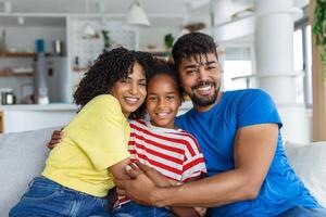 Love And Care. Portrait of cheerful family of three people hugging sitting on the sofa at home. Smiling young girl embracing her parents. photo