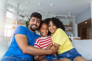 Portrait attractive multi-ethnic wife husband and kid indoors. Close up married couple with little pretty daughter sitting together smiling looking at camera. Concept friendly wellbeing happy family photo
