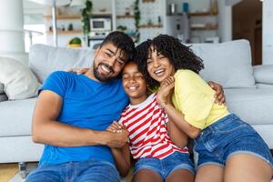 contento familia madre padre y niño hija riendo y teniendo divertido a hogar. contento africano americano familia relajante foto
