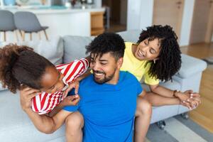 Attractive happy family hugging attractive mother handsome father and adorable small daughter sitting together on couch in living room at home smiling looking at camera photo