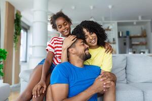 Portrait mother daughter and father sitting on couch at home. Adorable child embrace parents. Happy wellbeing multi-ethnic family concept photo