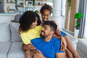 Attractive happy family hugging attractive mother handsome father and adorable small daughter sitting together on couch in living room at home smiling looking at camera photo