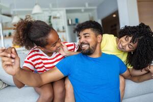 Attractive happy family hugging attractive mother handsome father and adorable small daughter sitting together on couch in living room at home smiling looking at camera photo